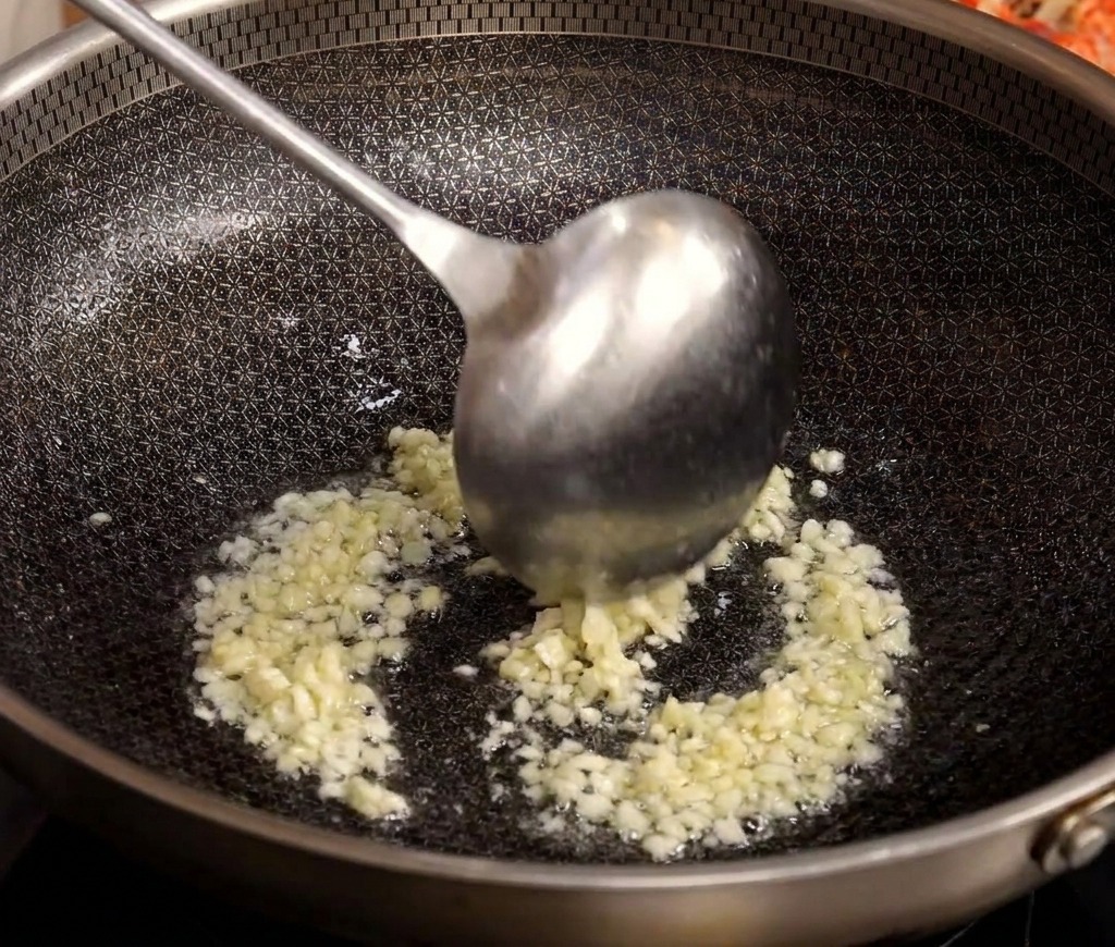 Une louche en métal remuant de lail haché qui crépite et dore dans un wok chaud avec de lhuile.