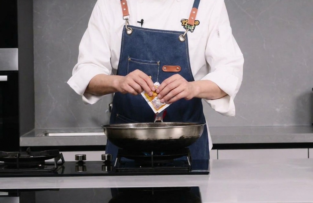 Une personne ouvrant un sachet de base de fondue chinoise épicée au-dessus dun wok.