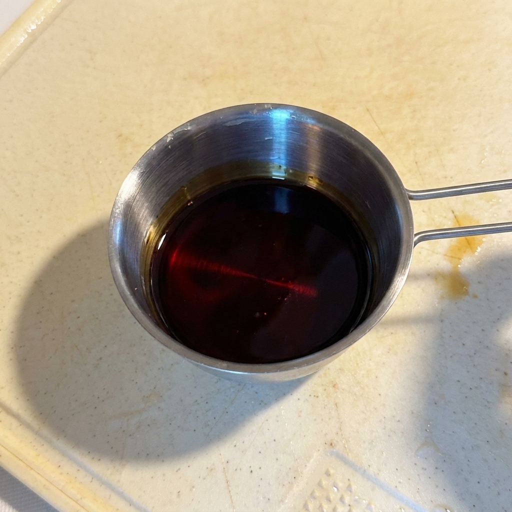 Un mélange de sauce sombre et brillante dans un petit récipient de mesure en inox.