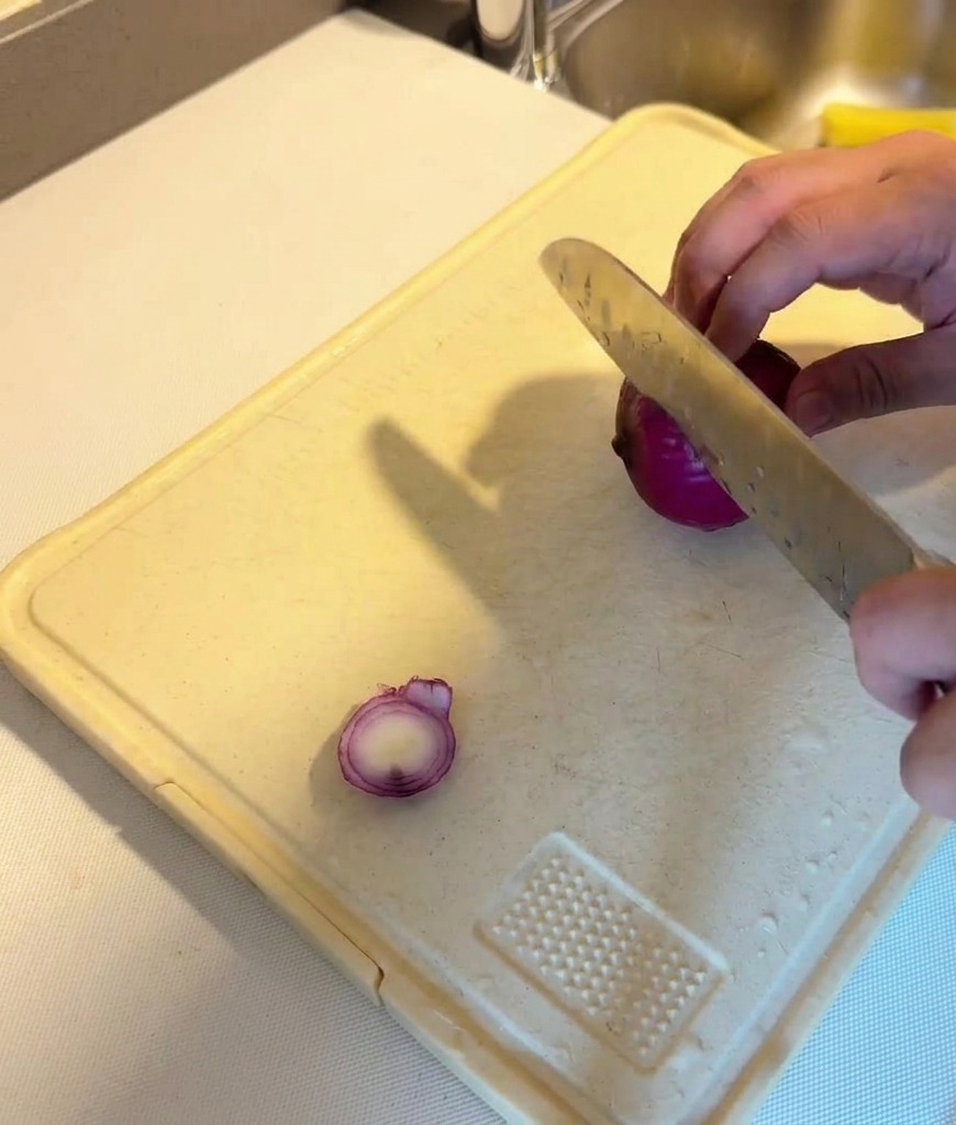 Découpe dun oignon rouge en fines lamelles régulières sur une planche à découper blanche.