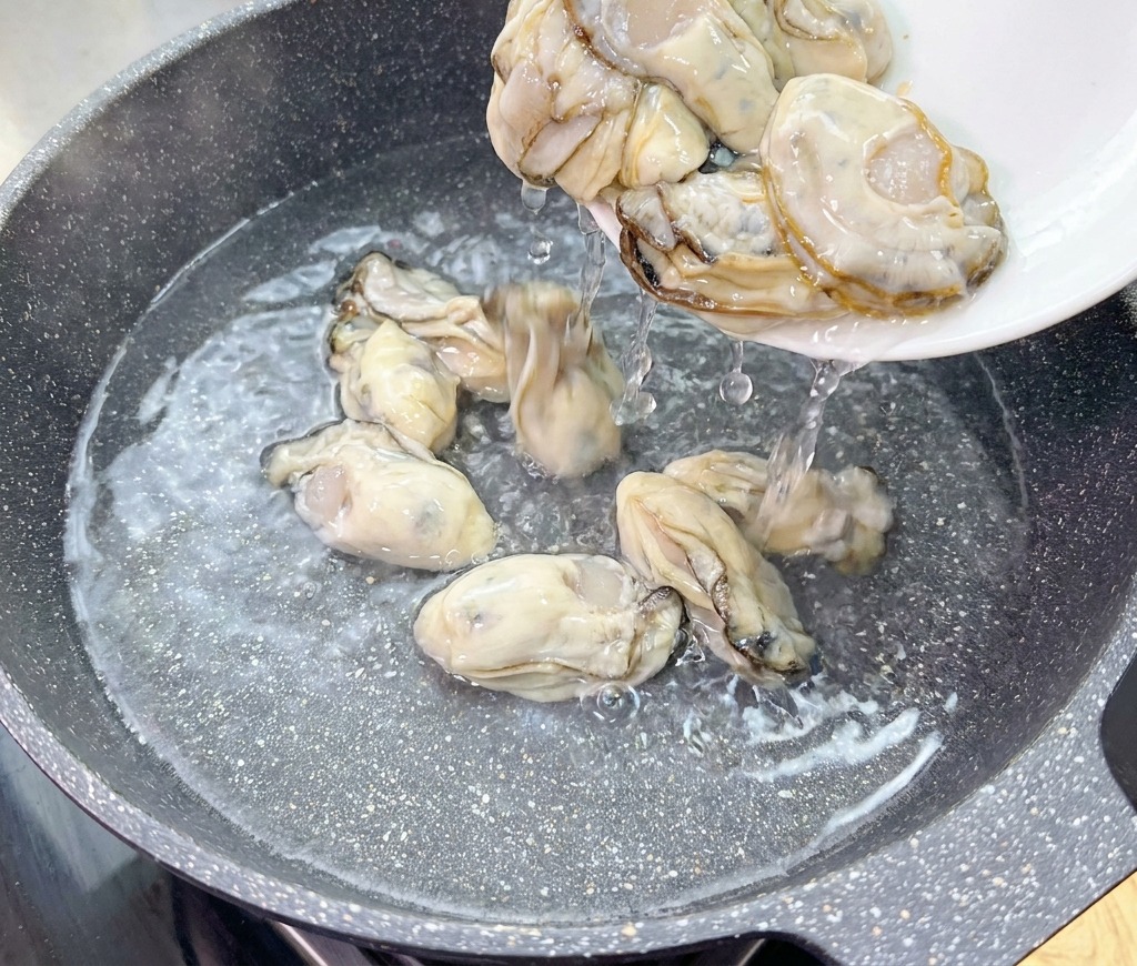 Des huîtres crues et charnues glissent dune assiette blanche vers un wok deau froide.