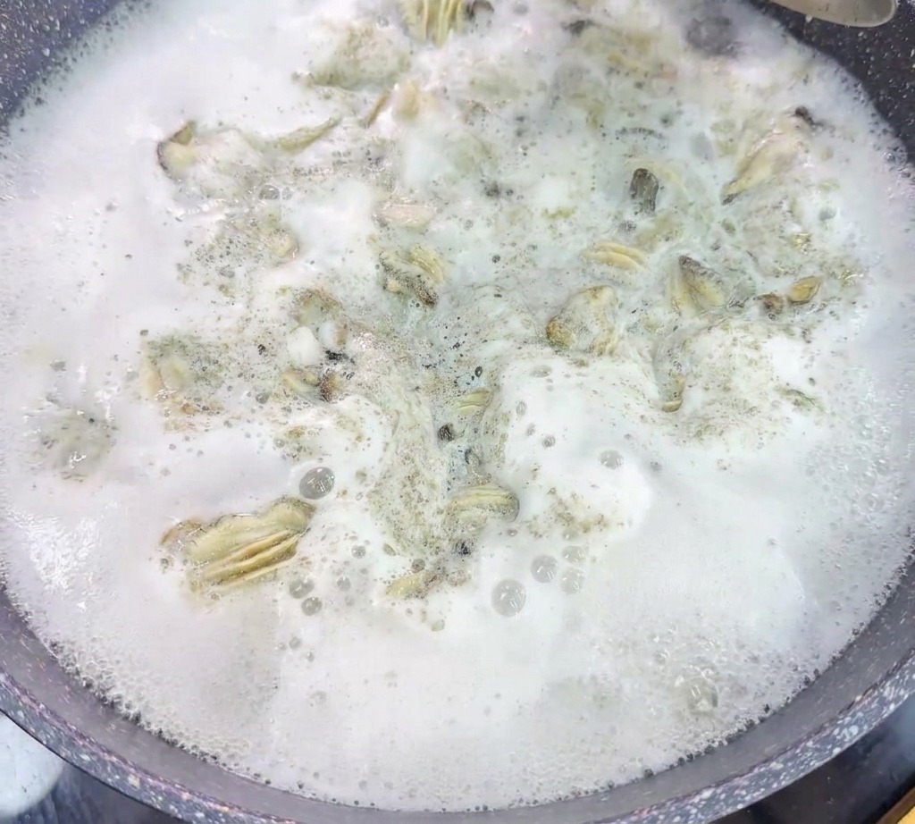 Une passoire en métal soulève les huîtres pochées dun wok deau bouillante et mousseuse.