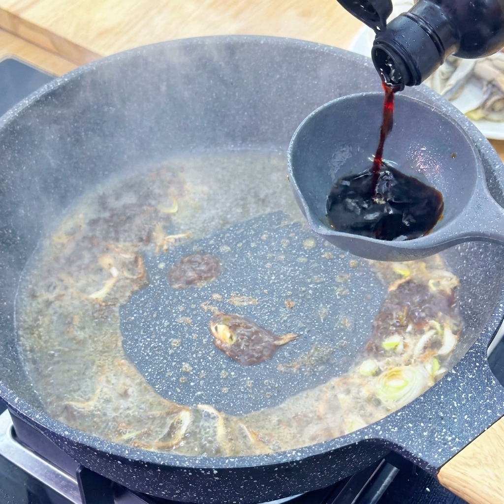 Sauce soja claire versée dune bouteille en verre sombre dans une louche grise au-dessus dune sauce frémissante.