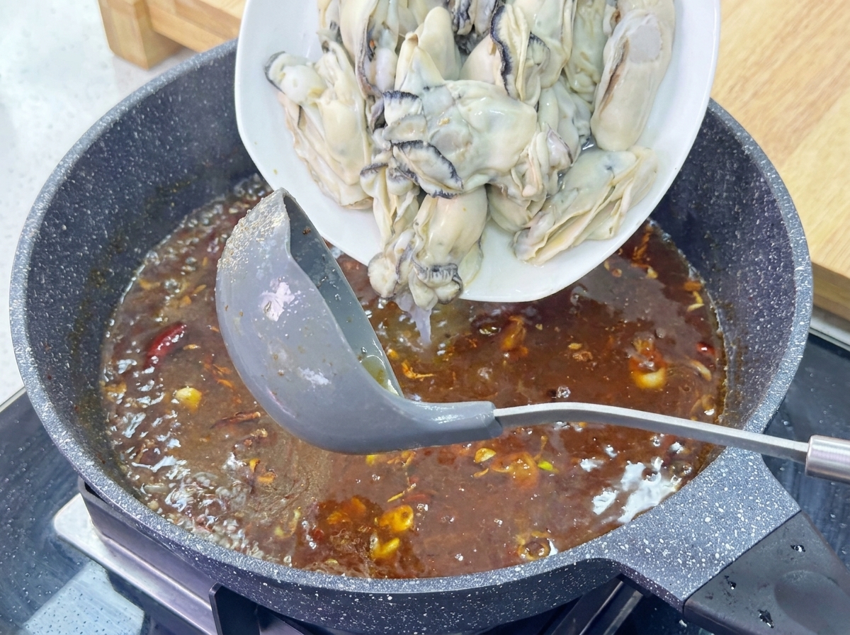 Une assiette dhuîtres charnues glissant dans une sauce brune bouillonnante dans une poêle en granit.