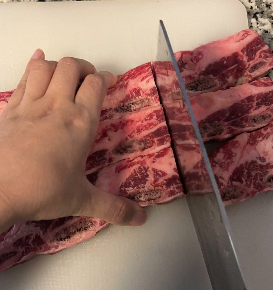 Une personne tranchant des travers de bœuf entre les os avec un couteau de chef sur une planche à découper blanche.