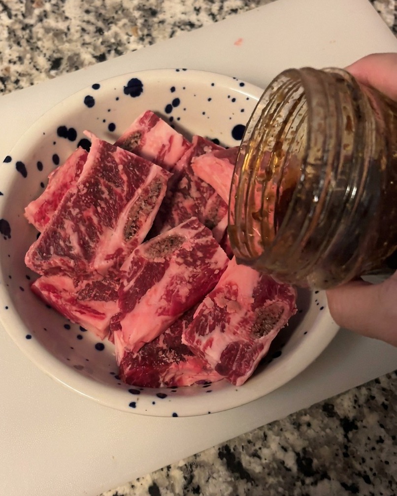 Sauce BBQ coréenne sombre et brillante versée depuis un bocal en verre sur des morceaux de bœuf dans un bol blanc moucheté de bleu.