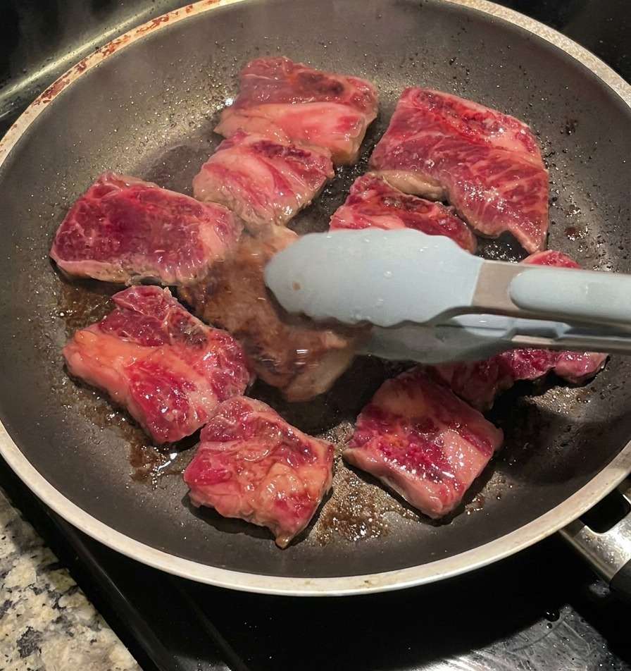 Utilisation dune pince pour retourner les travers de bœuf, révélant une croûte sombre et caramélisée sur la face cuite.