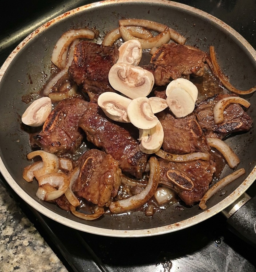 Champignons émincés sautés avec les travers de bœuf et les oignons caramélisés dans une poêle sombre.