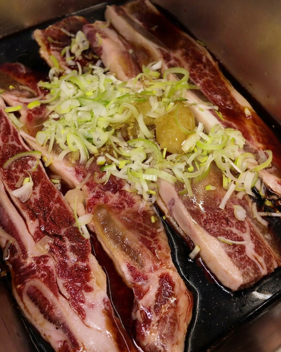 Huile de sésame grillée versée sur la marinade, créant une couche brillante sur le bœuf et les oignons.