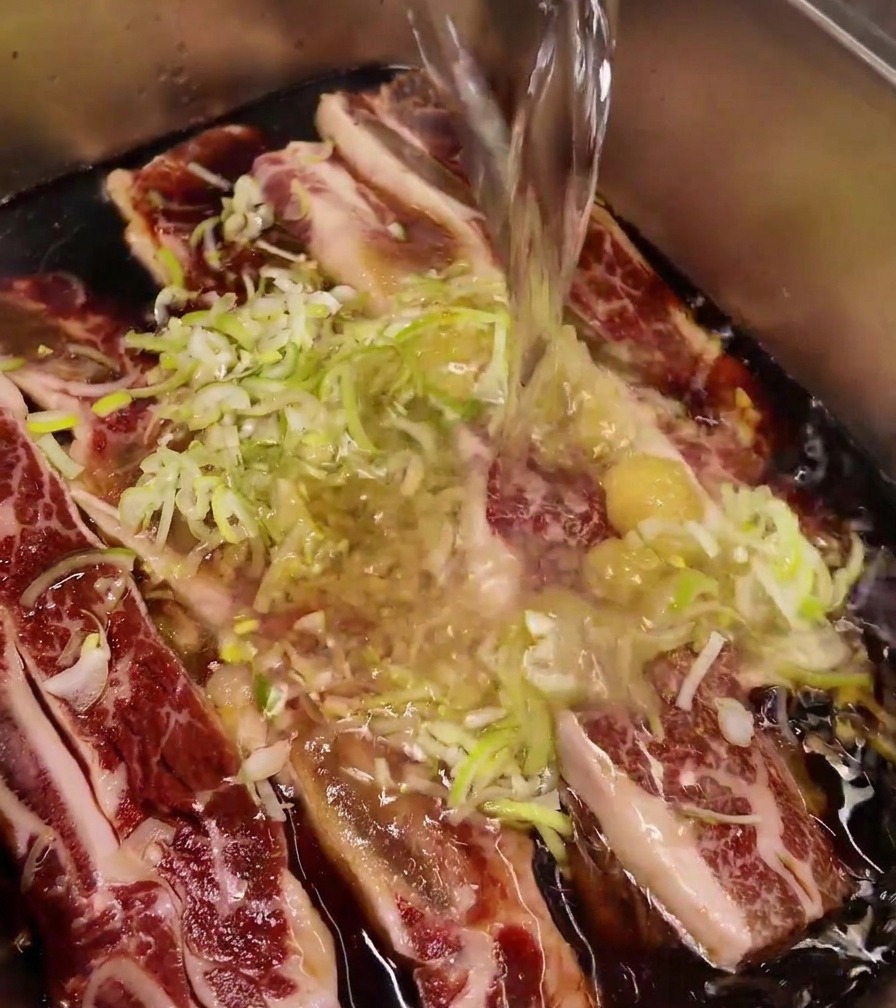 Jet deau claire versé dans un plat en inox contenant le bœuf, lail et les oignons verts.