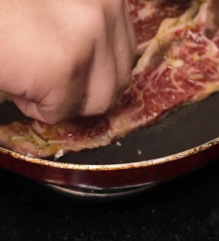 Main déposant une tranche de bœuf mariné dans une poêle antiadhésive bien chaude.