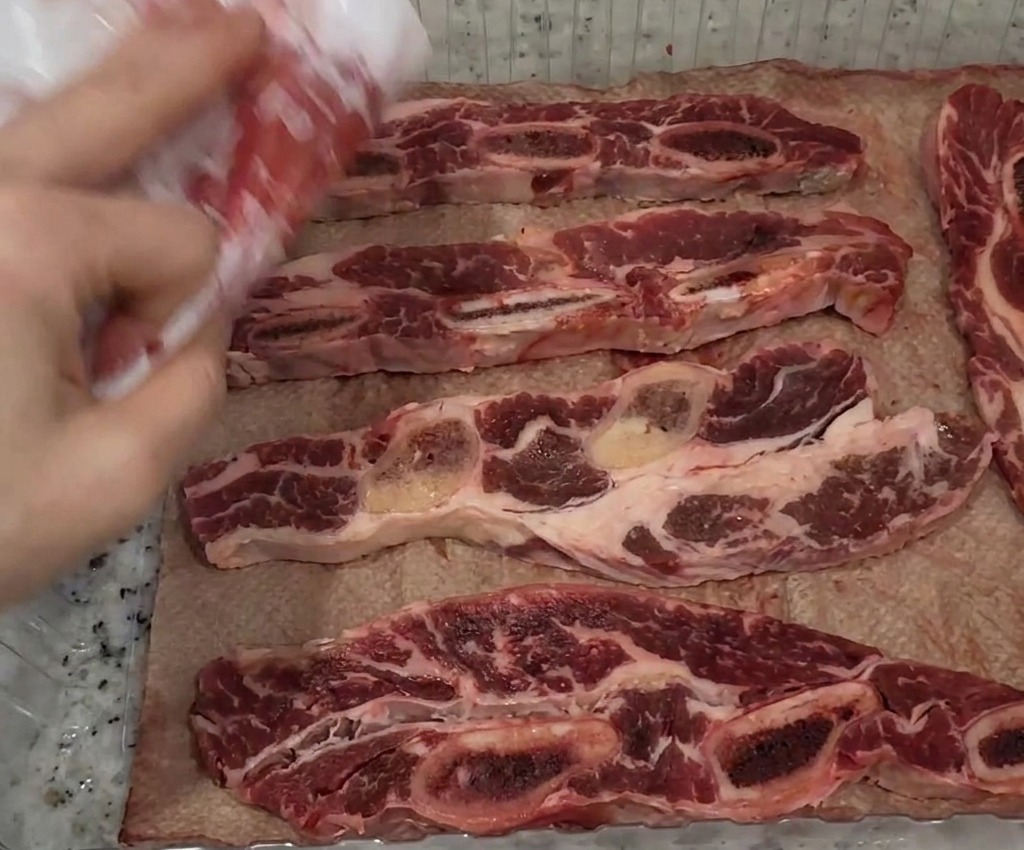Main utilisant du papier absorbant pour éponger des lanières de travers de bœuf crues dans un plateau.