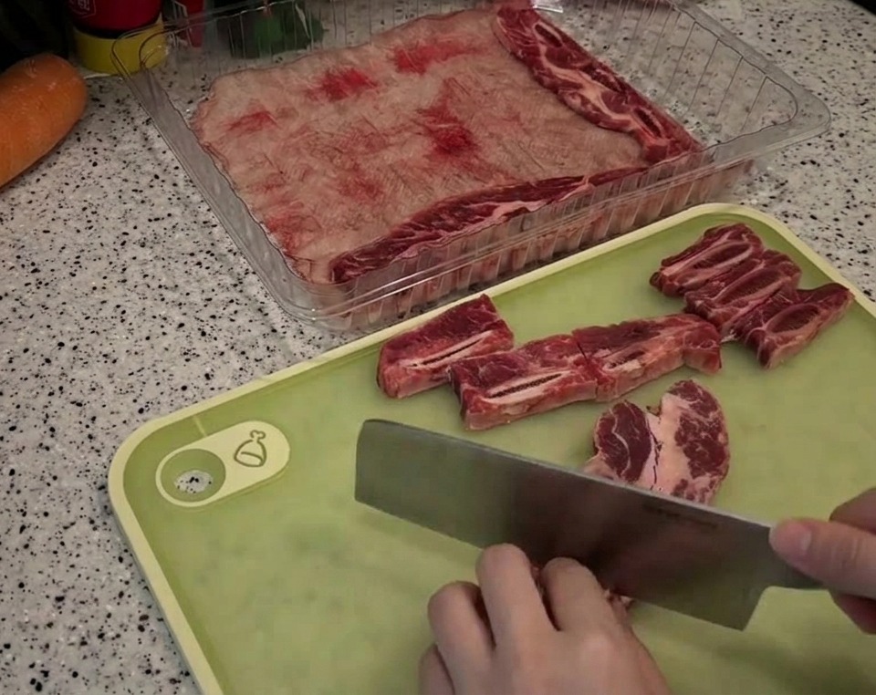 Utilisation dun couperet pour découper des travers de bœuf marbrés en petits morceaux rectangulaires sur une planche à découper.