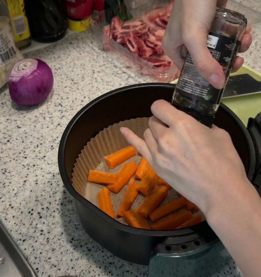 Moulage de poivre noir frais sur des bâtonnets de carottes crues dans le panier dun air fryer tapissé de papier.