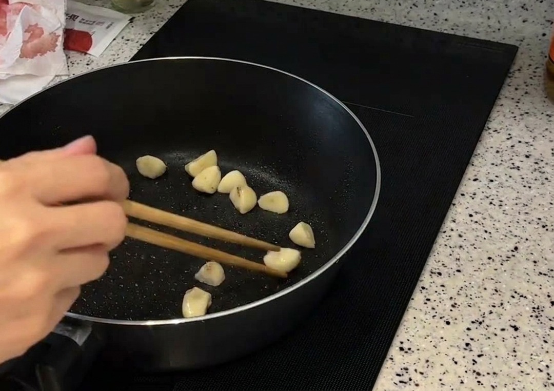 Gousses dail entières remuées avec des baguettes dans une poêle jusquà ce quelles soient dorées.