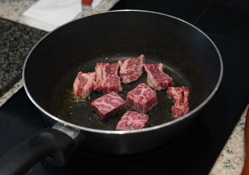 Morceaux de travers de bœuf marbrés saisissant dans une poêle sombre, les bords devenant bruns.