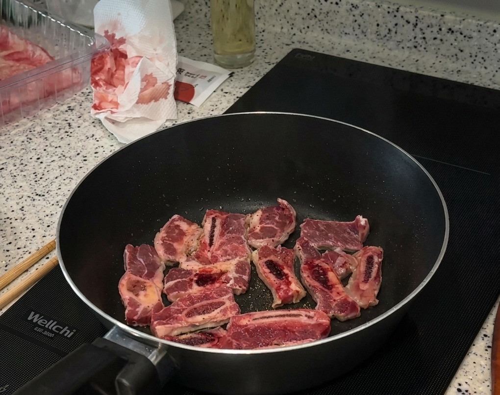 Morceaux de bœuf grillant dans une poêle noire sur une plaque à induction, avec sel et poivre bien visibles.