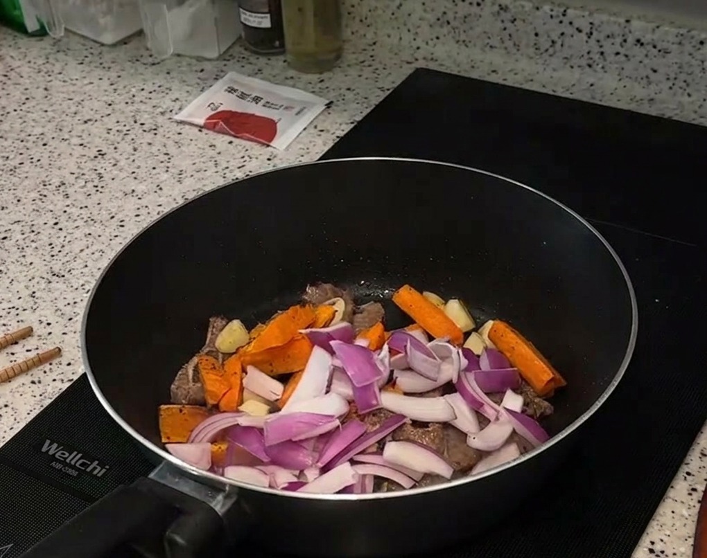 Lamelles doignon rouge et bâtonnets de carottes rôties ajoutés sur les morceaux de bœuf saisis dans la poêle.
