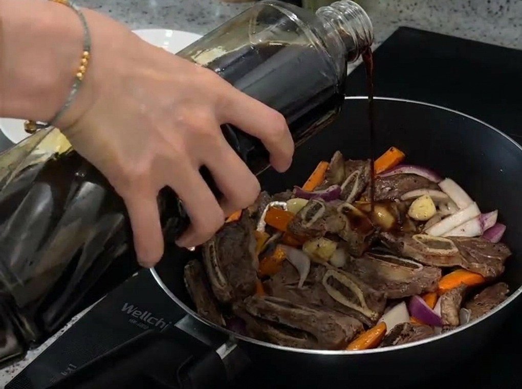 Gros plan de sauce soja claire versée dune bouteille dans une poêle contenant du bœuf, des carottes et des oignons.