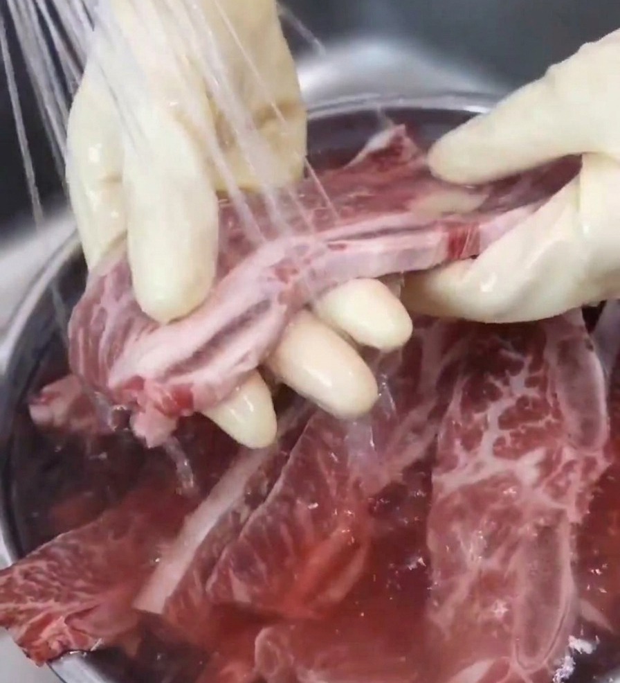 Une main gantée rince un morceau de bœuf sous un filet deau fraîche au-dessus dun évier.