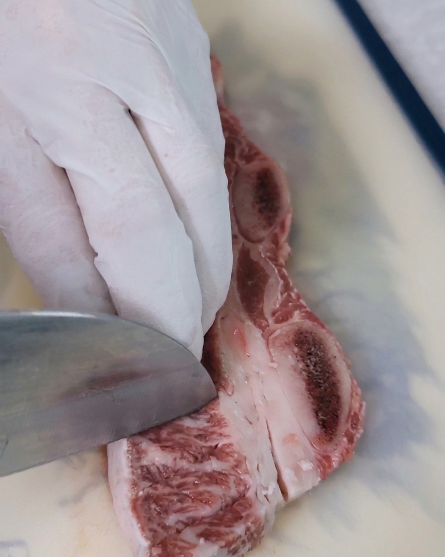 Gros plan sur une lame de couteau traçant des losanges dans la chair rouge du bœuf.