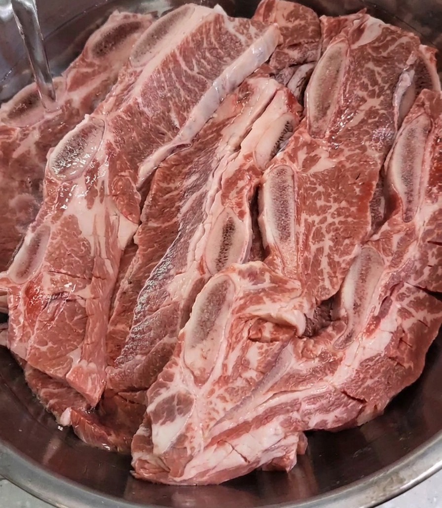 De leau claire est versée dans un bol en inox rempli de travers de bœuf jusquà les recouvrir totalement.
