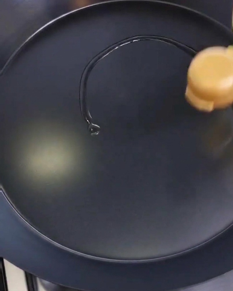 Une personne étale un mince film dhuile sur une poêle noire à laide dun papier absorbant plié.