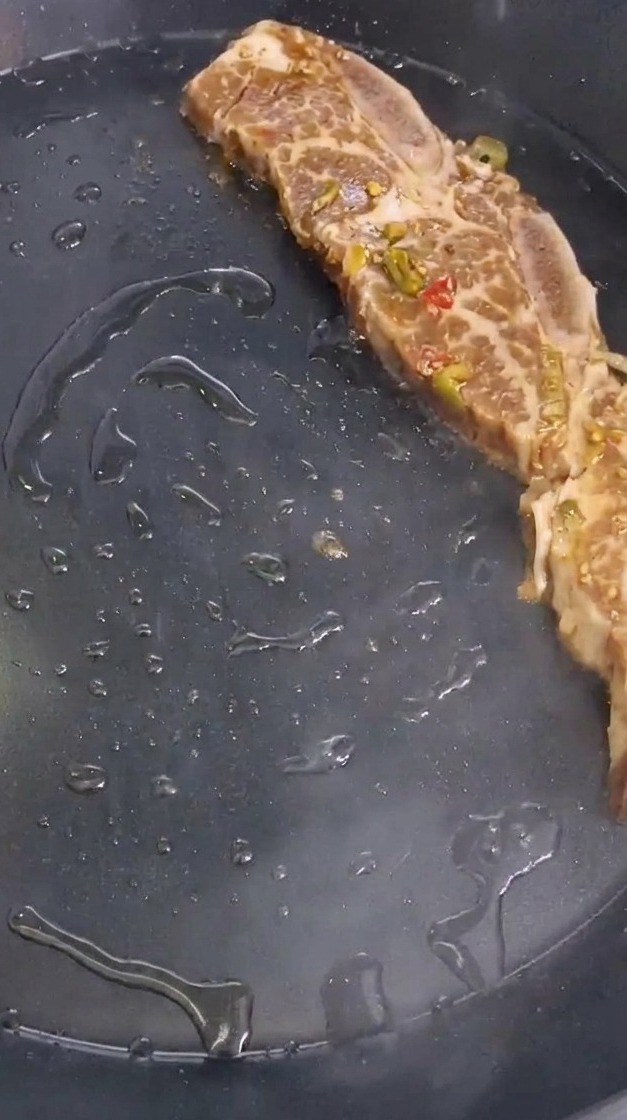 Un morceau de travers de bœuf mariné avec des éclats de piment est déposé dans une poêle chaude.