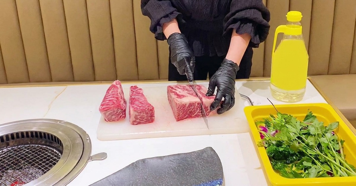 Une personne portant des gants noirs utilise un couteau de chef pour diviser une grosse côte de bœuf crue persillée en sections rectangulaires.