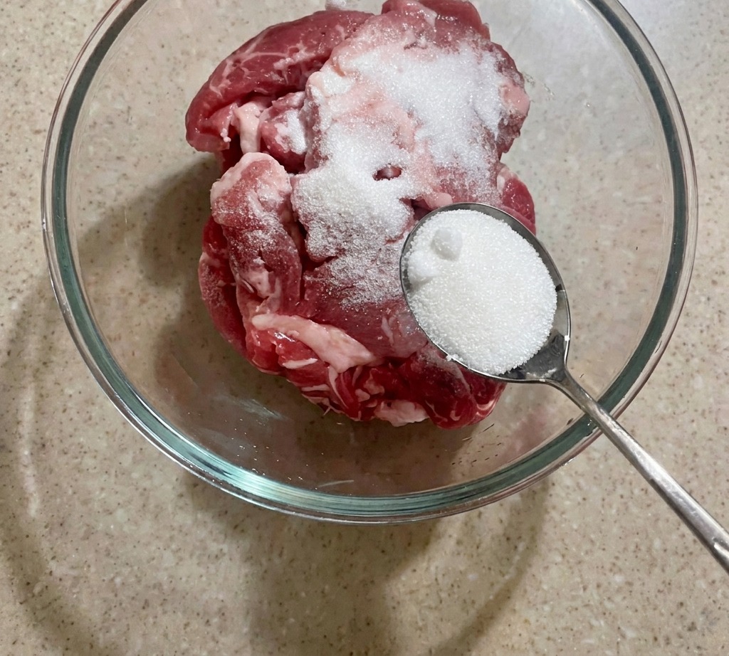 Un bol de tranches de porc crues que lon saupoudre de sucre blanc.
