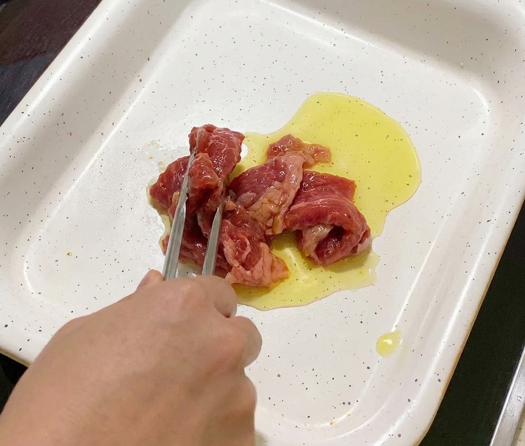 Tranches de porc mariné déposées à laide dune pince dans une poêle chaude huilée.