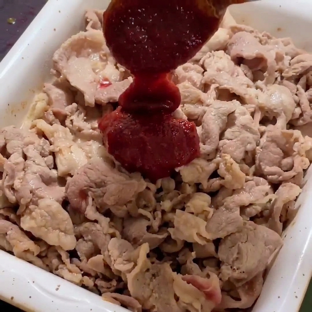 Ajout de la sauce rouge épicée sur le porc en train de grésiller dans la poêle.