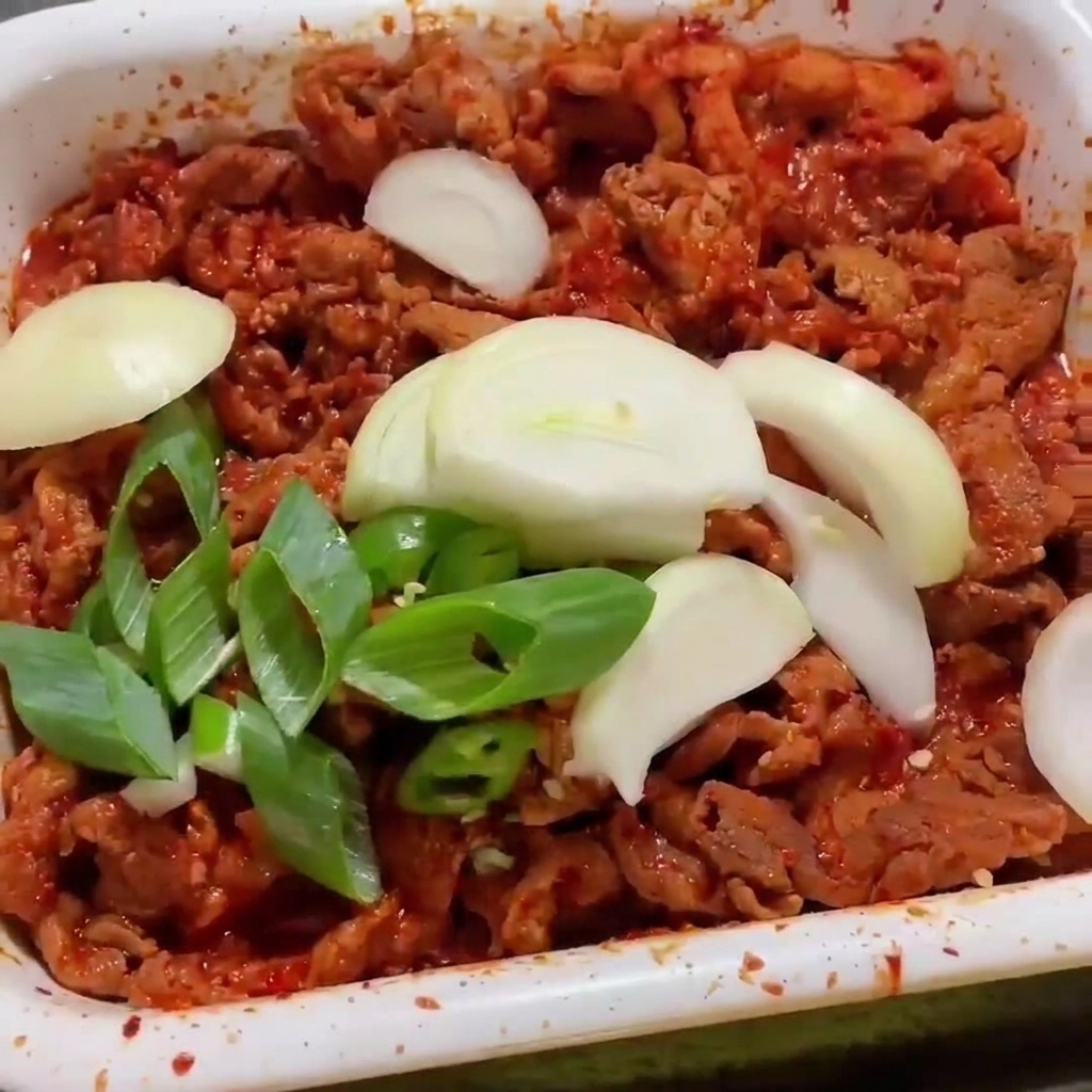 Oignons et piments frais ajoutés par-dessus le porc pimenté dans la poêle blanche.