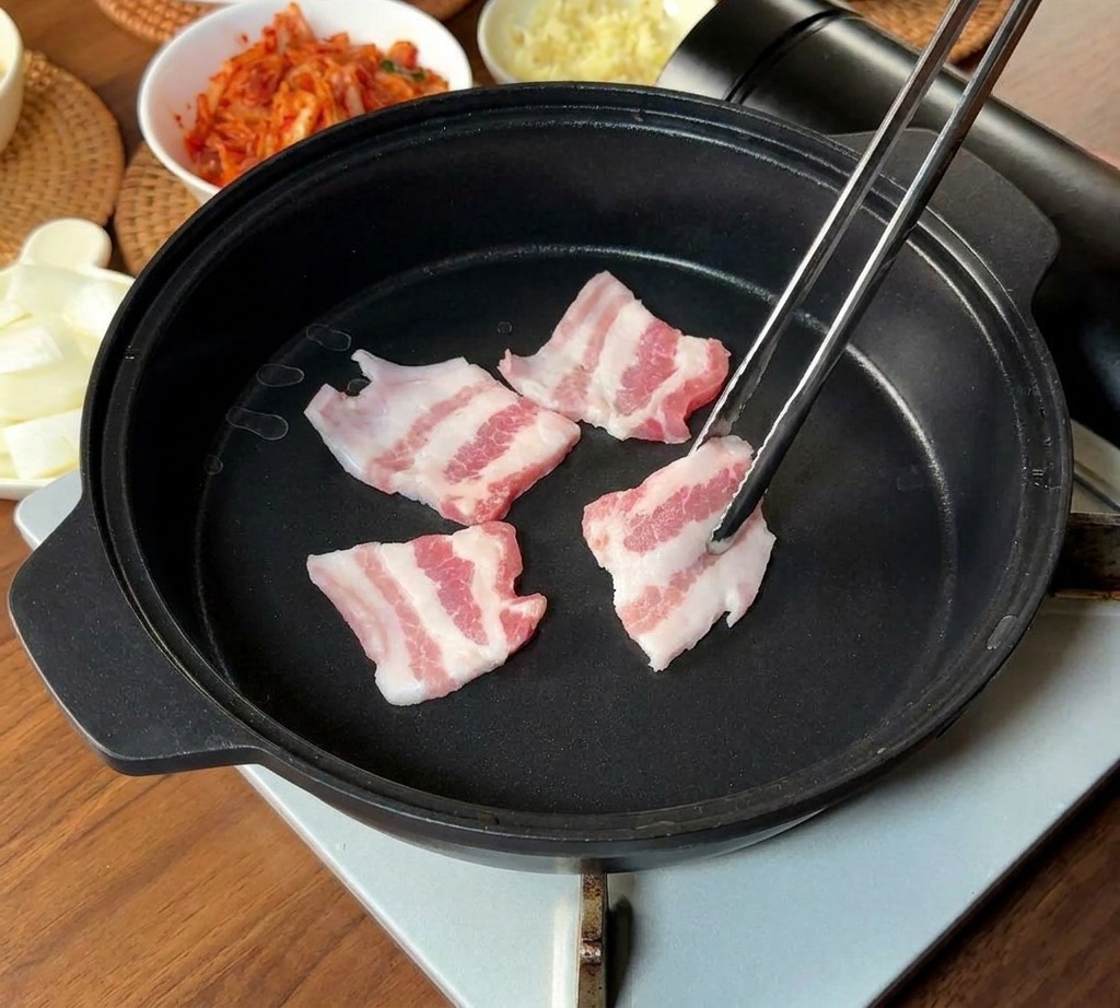 Fines tranches de porc marbrées déposées dans une poêle noire avec des baguettes en métal.