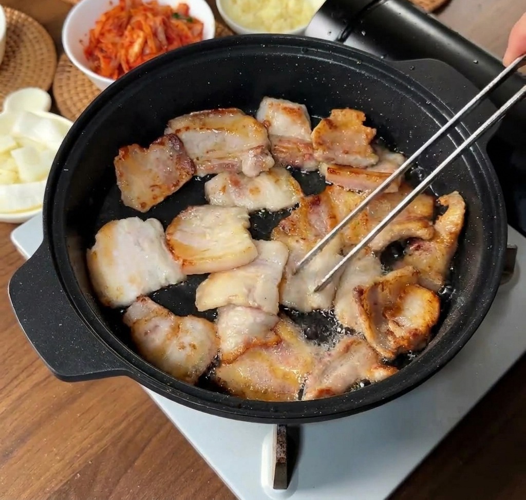 Tranches de porc dorant dans leur propre graisse dans une poêle, certaines étant retournées avec une pince.