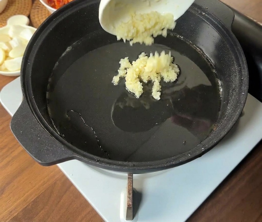 Ail haché versé au centre dune poêle chaude contenant le gras de cuisson du porc.