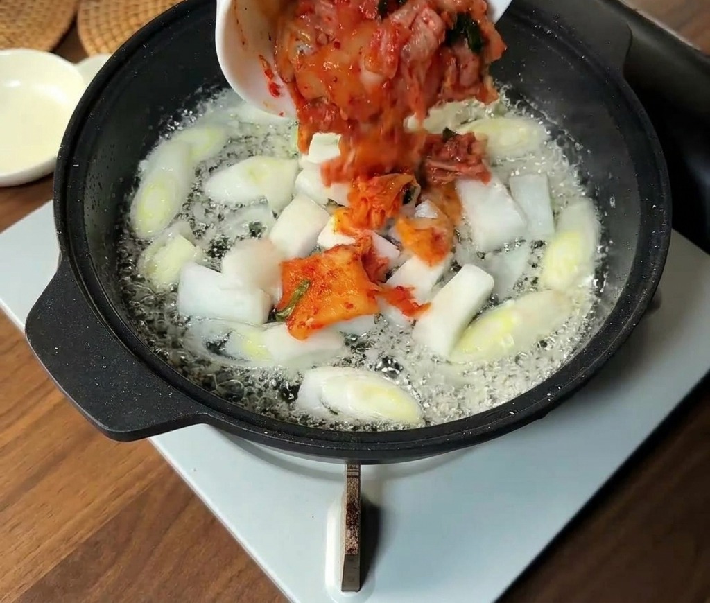 Kimchi haché et tranches doignon blanc ajoutés aux aromates dans la poêle.