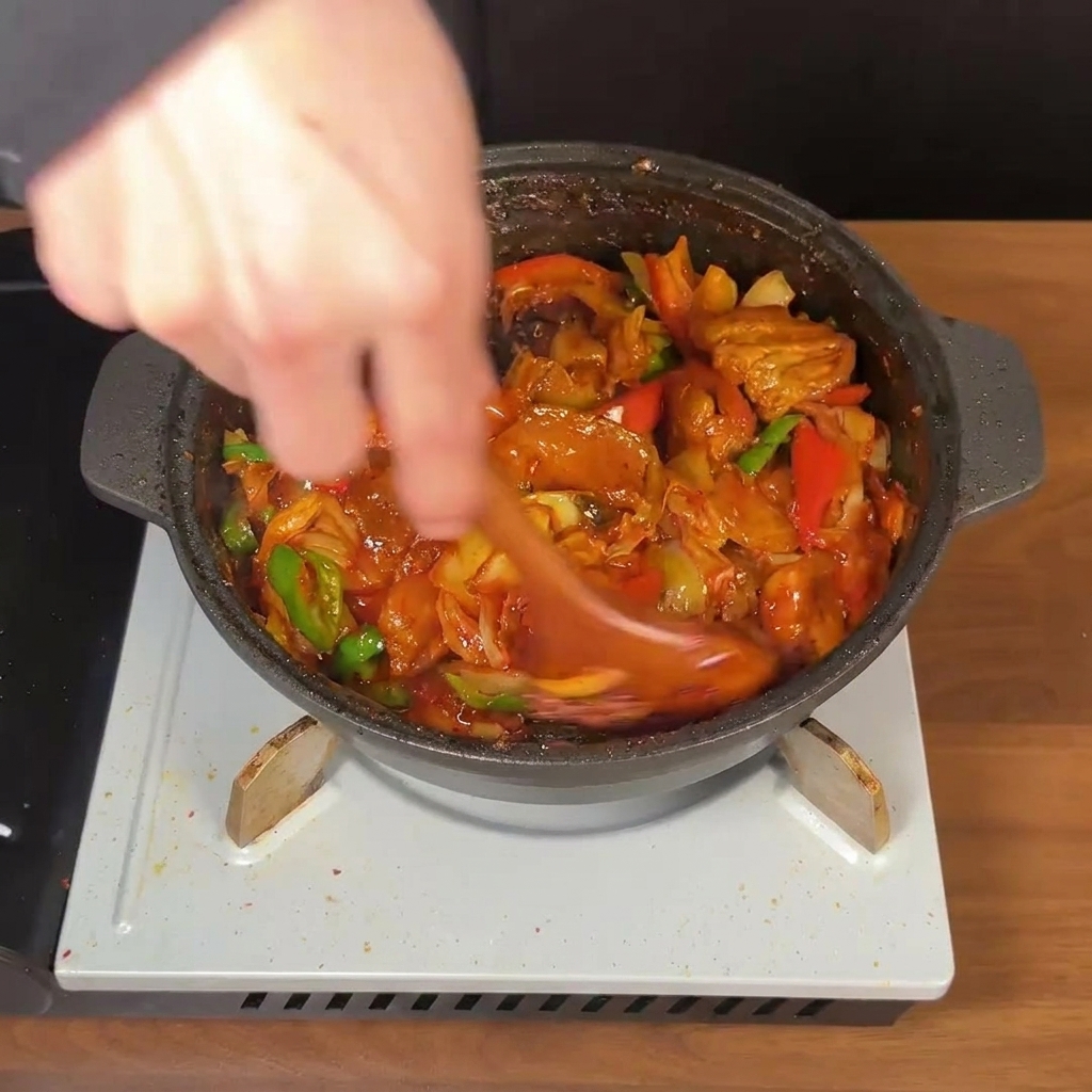 Cuillère en bois mélangeant vigoureusement le porc épicé et le kimchi dans une sauce rouge brillante.