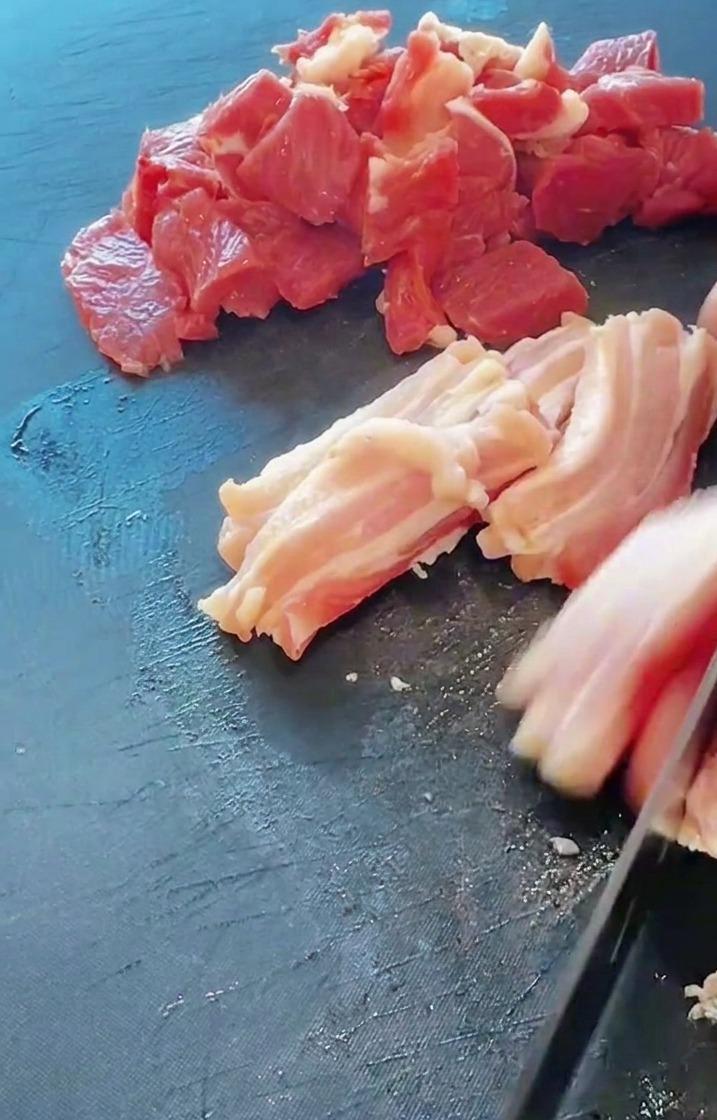 Gros plan dun couteau tranchant de la poitrine de porc fraîche sur une planche à découper sombre.