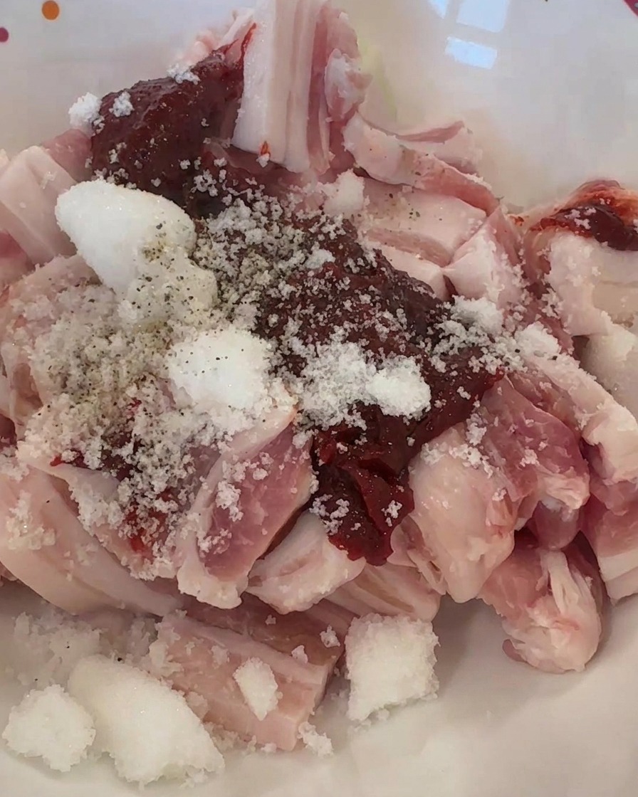 Lamelles de porc cru dans un bol garnies de pâte de piment rouge, de sucre blanc et de poivre noir.