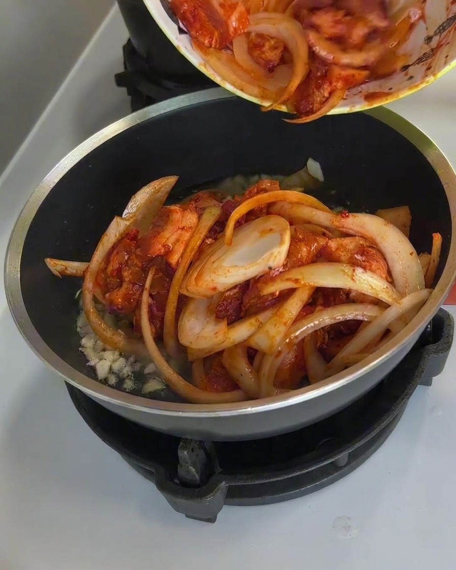 Porc épicé et oignons cuisant dans une poêle avec de la vapeur et une sauce caramélisée bouillonnante.