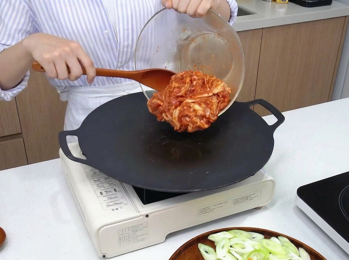 Poitrine de porc marinée déposée sur une plaque de cuisson chaude à laide dune spatule.