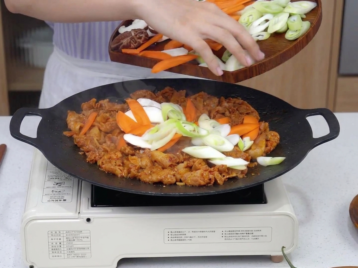 Légumes tranchés ajoutés à la viande épicée qui grille dans une poêle.