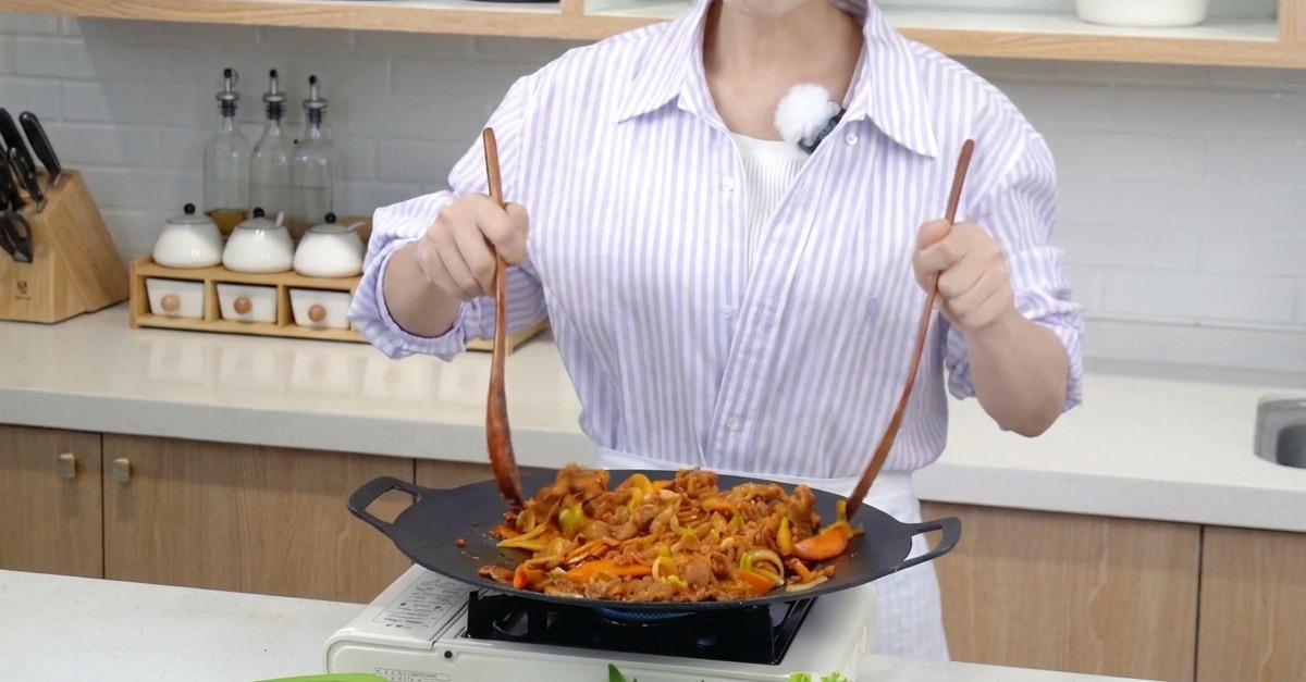 Porc et légumes colorés sautés énergiquement dans une poêle avec deux spatules en bois.