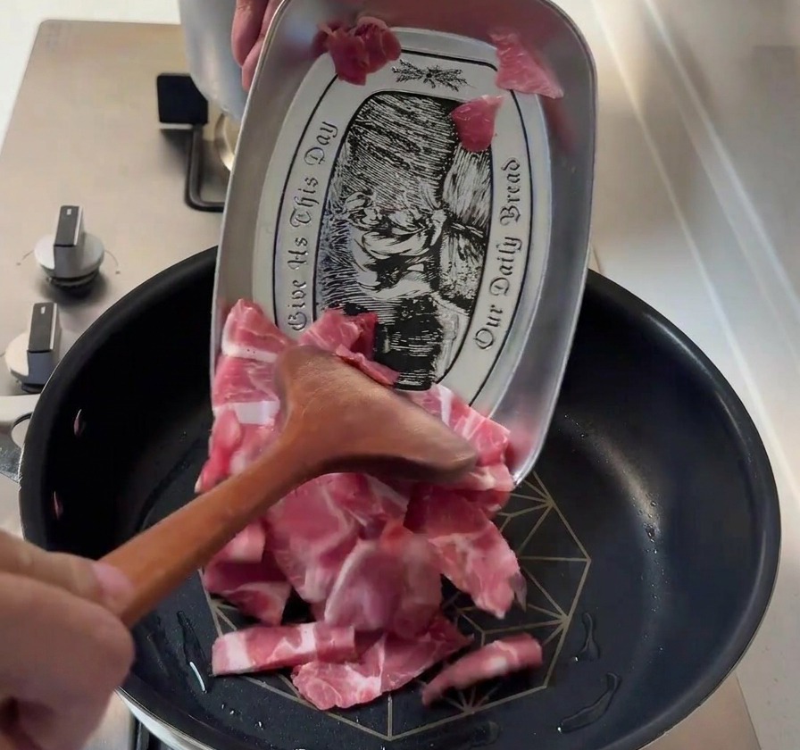 Tranches dépaule de porc crues ajoutées dans une poêle chaude à laide dune spatule en bois.