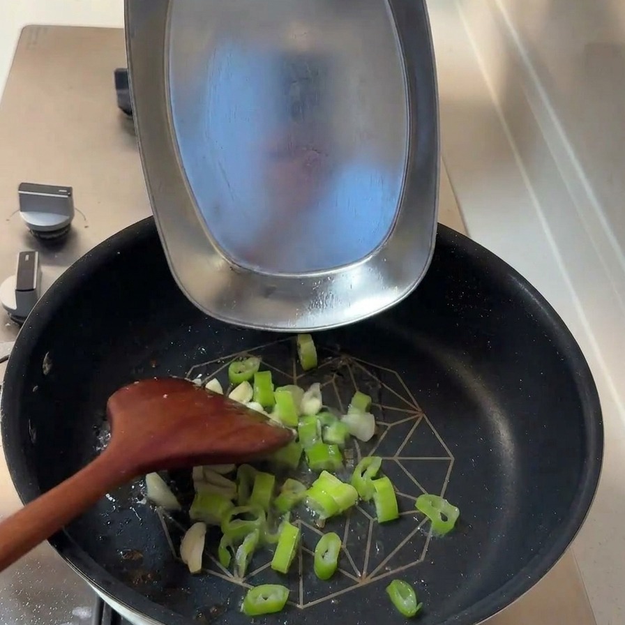 Oignons verts hachés et lamelles dail frais ajoutés dans la poêle avec les sucs de cuisson.
