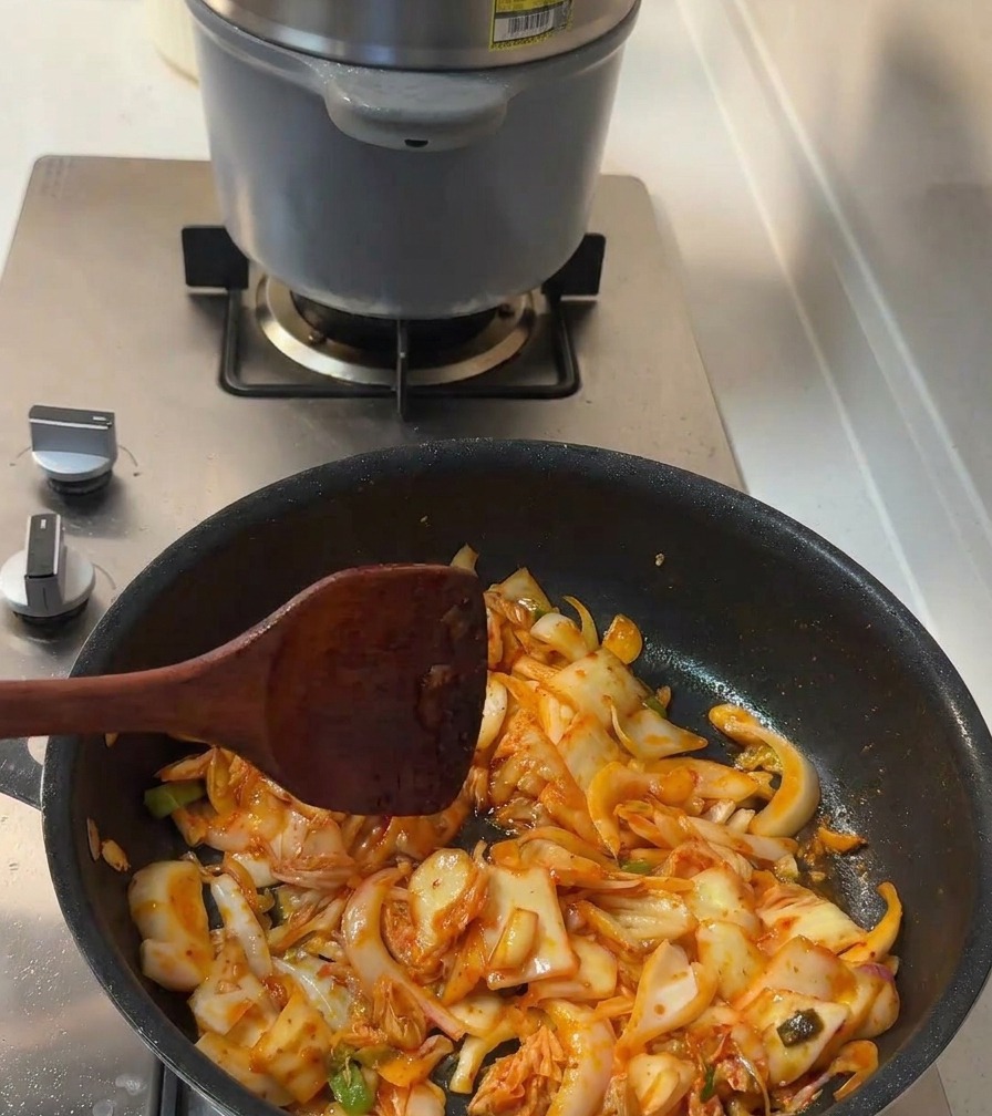Sauce soja et sucre blanc versés sur le mélange de kimchi et doignons en cuisson.