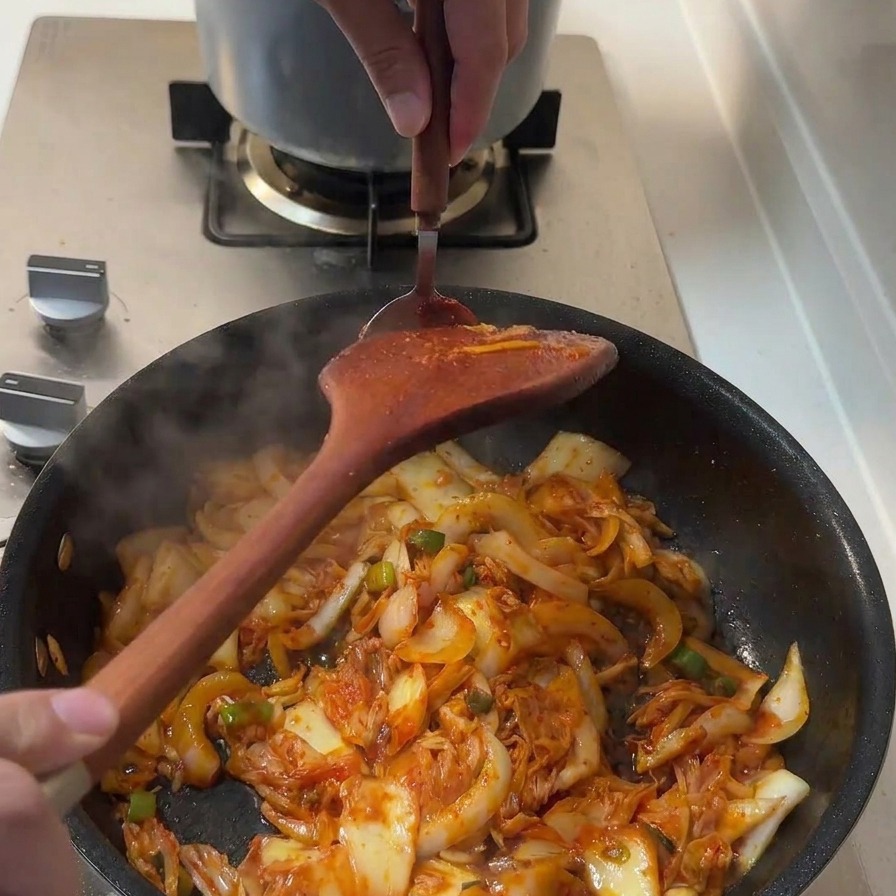 Une cuillerée de pâte gochujang épaisse et rouge ajoutée dans la poêle de sauté.