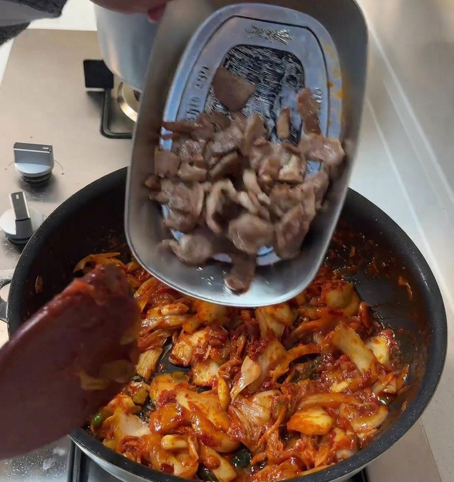Tranches de porc saisies reversées dans la poêle contenant la base de kimchi épicée.