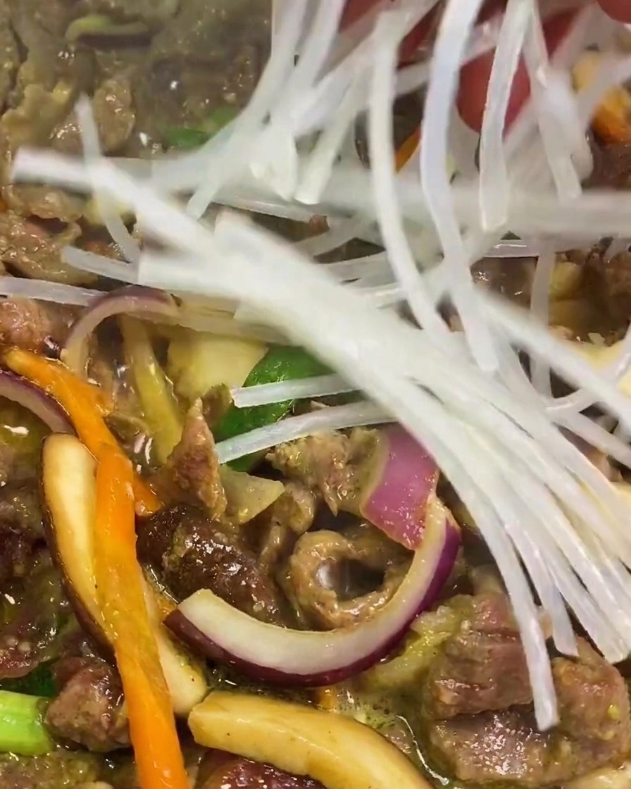 Une main déposant un paquet de nouilles de fécule de patate douce claires et trempées dans une poêle de bœuf et de légumes frémissants.